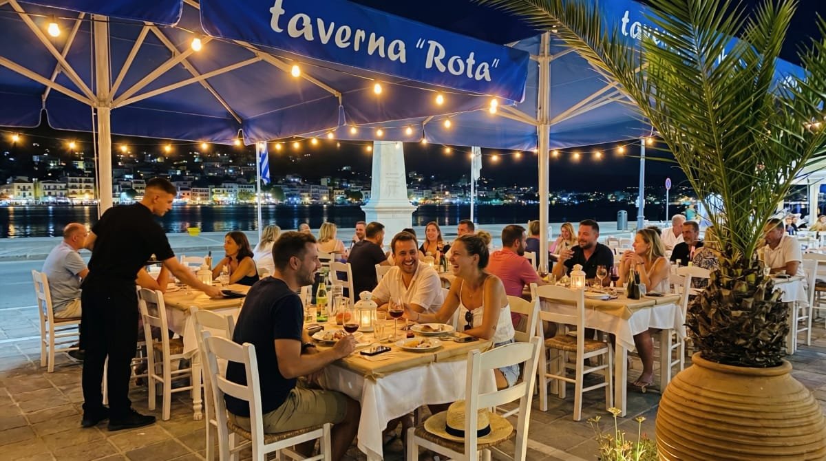 Dinner beneath the Taverna Rota awning with Poros harbor lights behind the tables.